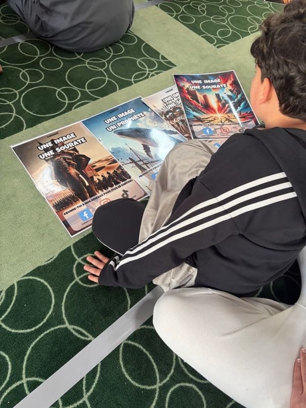 Un enfant assis sur le tapis d’une mosquée devant des affiches « Une image, une sourate » et « Une image, un prophète »