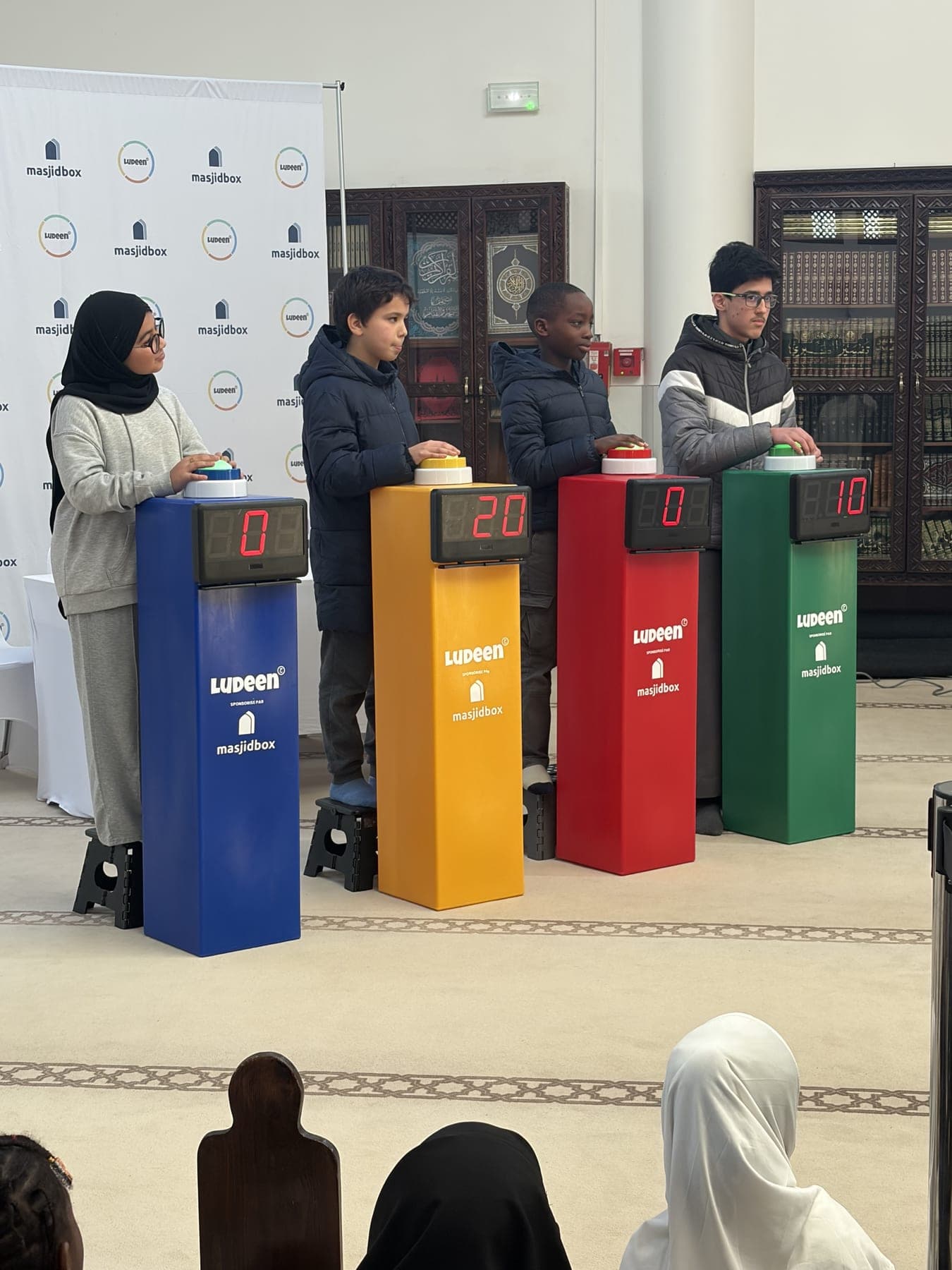 Quatre enfants derrière des pupitres de couleur, la main sur leur buzzer, pendant la finale d’un Quiz des Mosquées